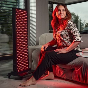 Alt texty – galéria: 1. Žena sedí pri svetelnom paneli MITO LIGHT® na stojane Floor Stand 5.0 – terapia červeným svetlom v obývačke v sede