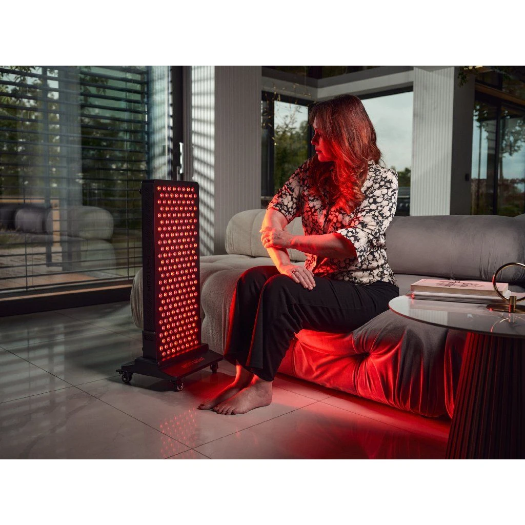 stojan-mito-light-floor-stand-5-0-9 Žena sedí na gauči a ohliada si ruku pri svetelnom paneli MITO LIGHT® na stojane Floor Stand 5.0 – terapia červeným svetlom