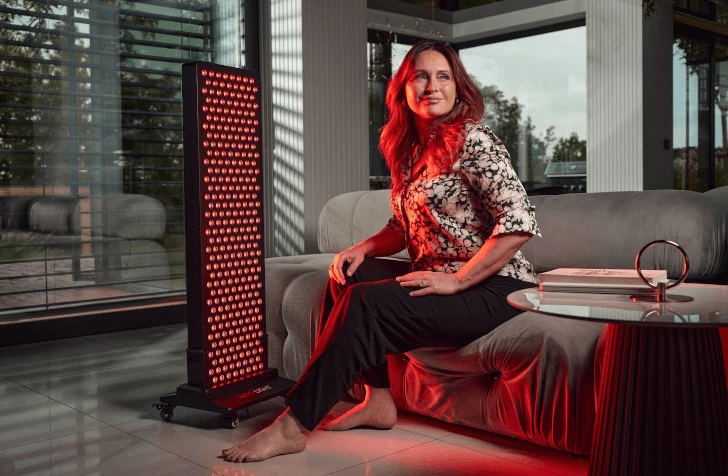 Žena sedí pri svetelnom paneli MITO LIGHT® na stojane Floor Stand 5.0 – komfortná terapia červeným svetlom kdekoľvek doma