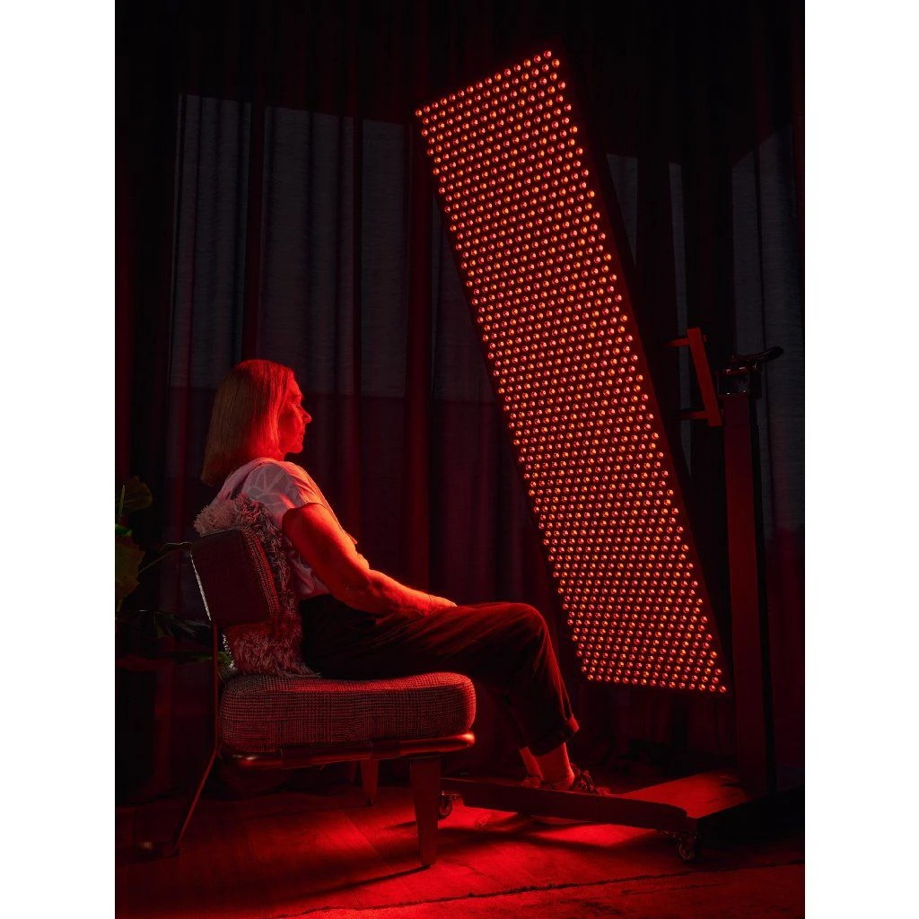 stojan-mito-light-lift-stand-max-7 Žena sedí na stoličke pri svetelnom paneli MITO LIGHT® v šikmej polohe na stojane Lift Stand Max – terapia červeným svetlom v sede