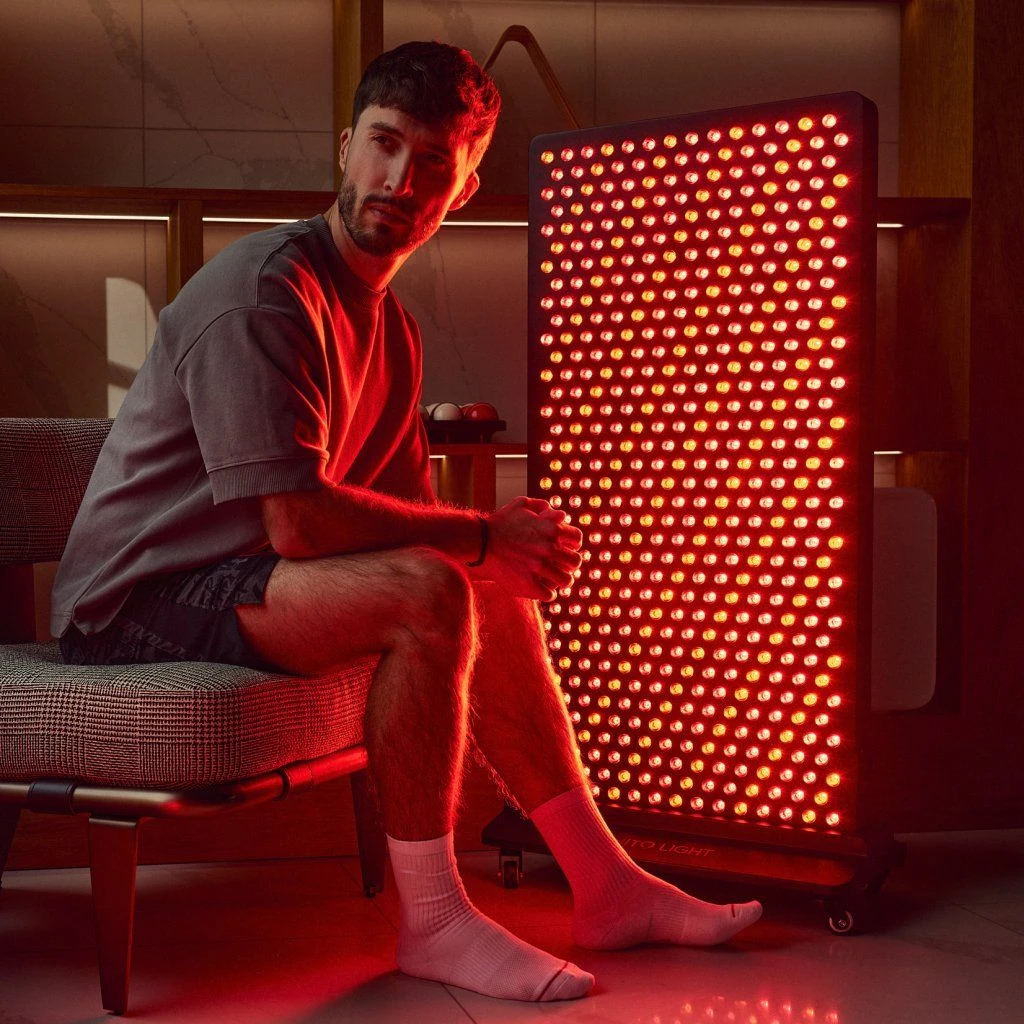 Muž sedí na stoličke pri paneli MITO LIGHT® Mitohacker 5.0 na stojane Mitohacker Floor Stand 5.0 – terapia červeným svetlom v sede