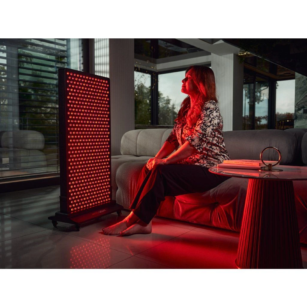 stojan-mito-light-mitohacker-floor-stand-5-0-3 Žena sedí na gauči pri paneli MITO LIGHT® Mitohacker 5.0 na stojane Mitohacker Floor Stand 5.0 – terapia červeným svetlom v obývačke